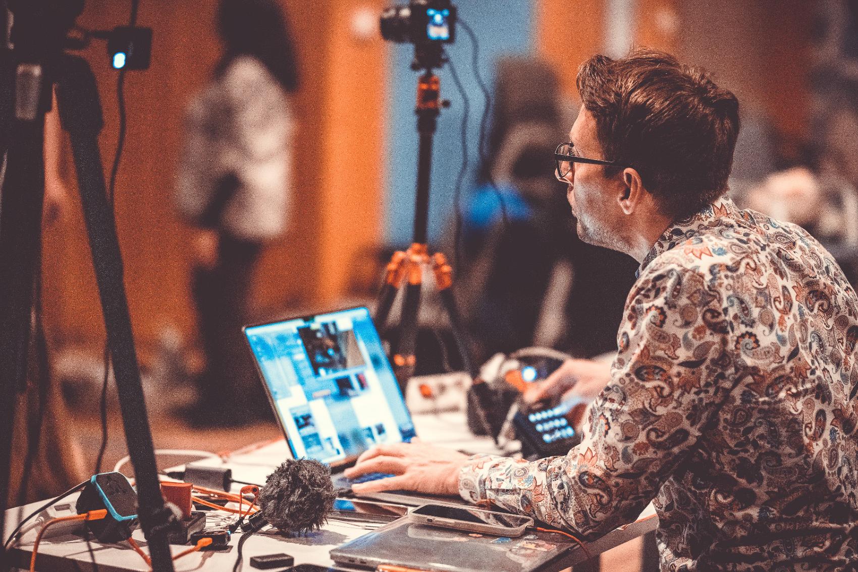 Technicien de diffusion à un ordinateur portable avec logiciel de streaming multi-caméra, caméras et microphones lors d'un événement en directn, le couple sur scène devant un public assis et des compositions florales -caméra sur ordinateur portable avec stream deck